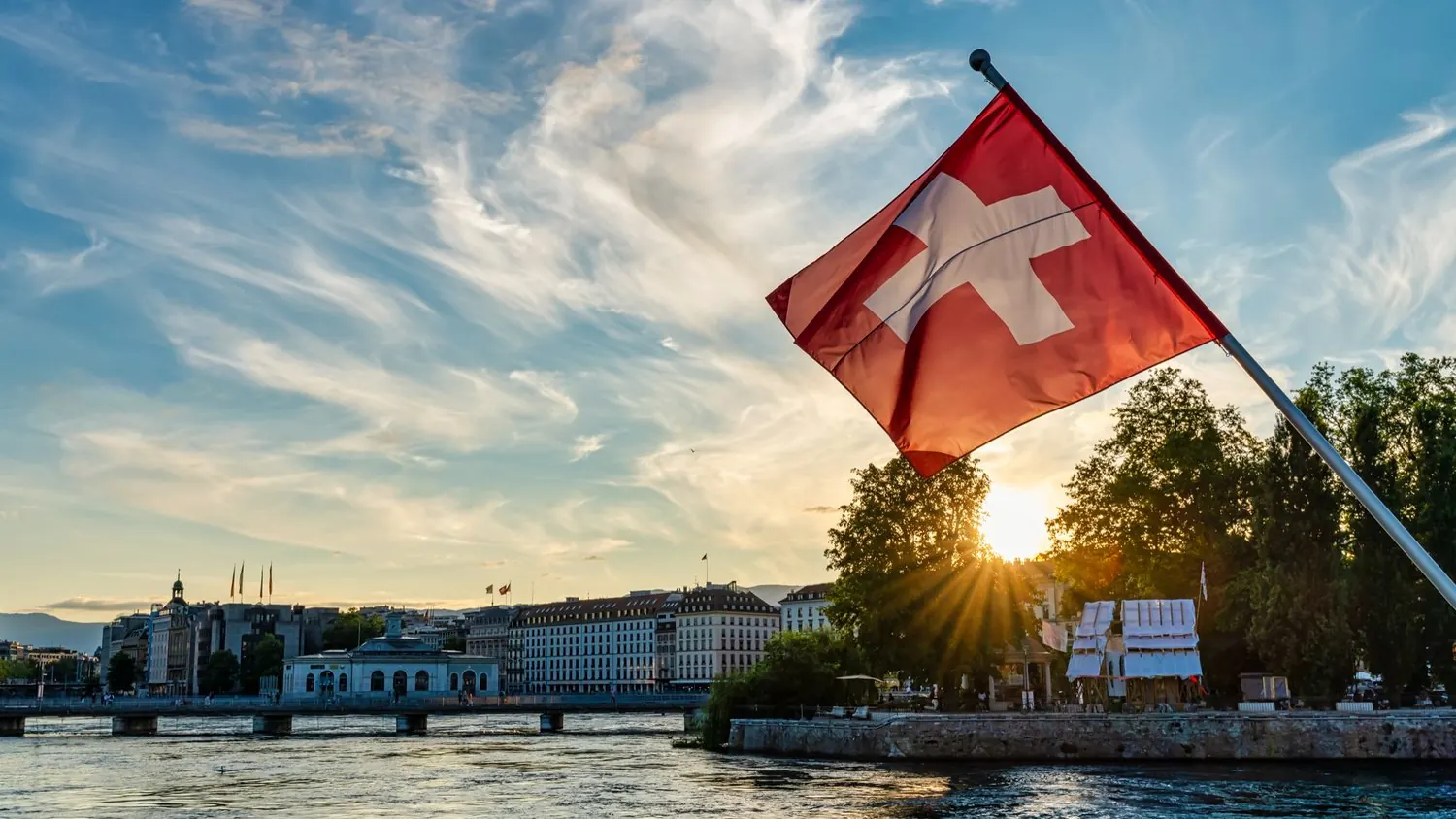 Schweizer Fahne im Abendlicht über einer Stadt am Wasser
